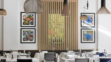 A restaurant with tables set for dining, framed artwork on the walls, and hanging pendant lights.