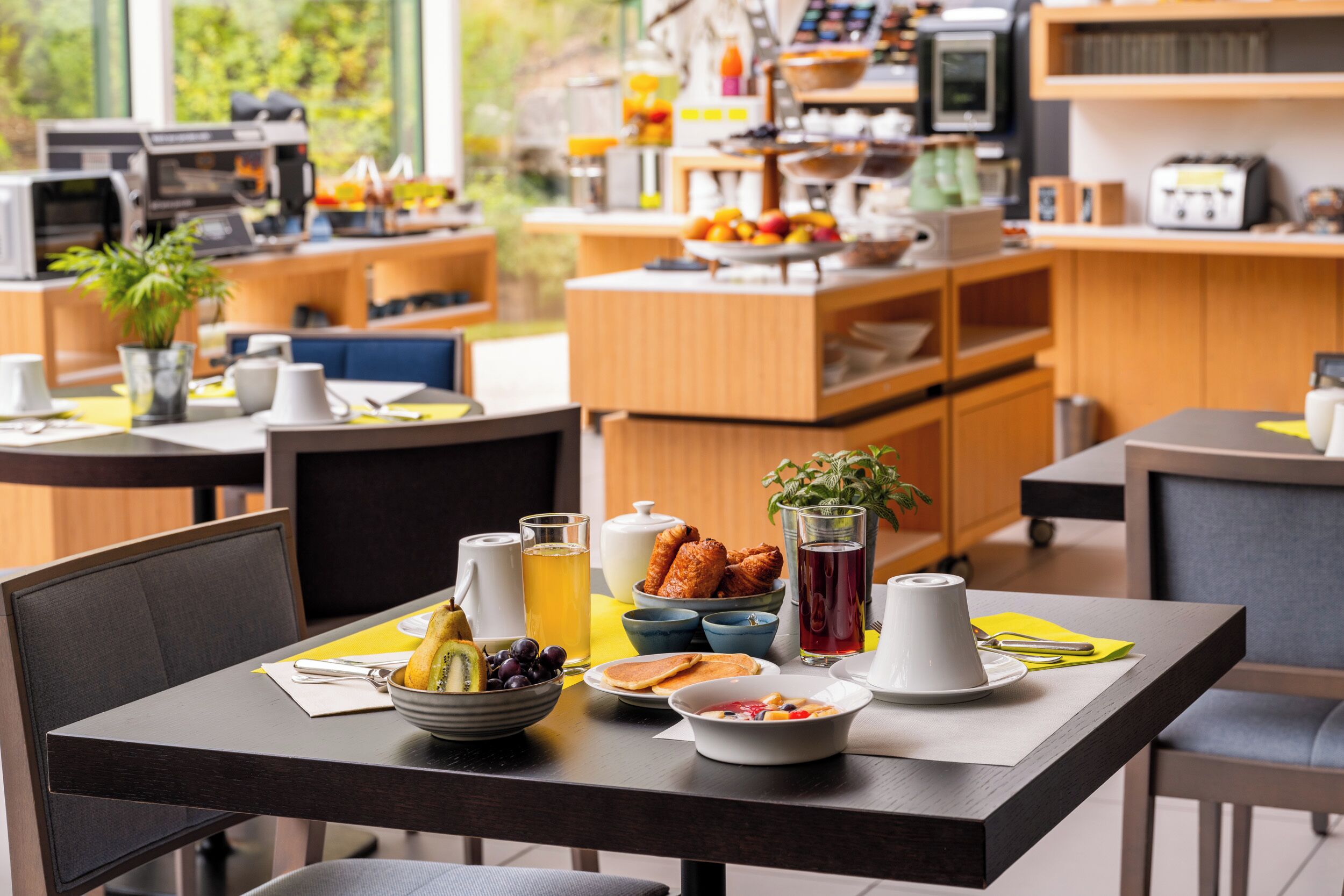 Desayuno listo para dos personas, con una mesa que incluye un bol de fruta, una tetera y una jarra de jugo.