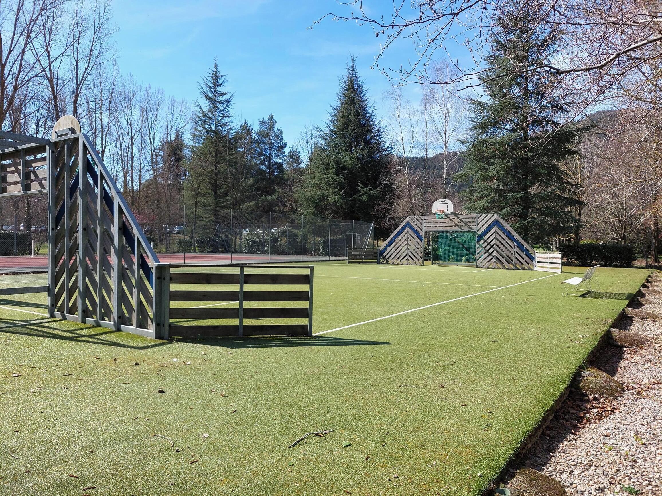 A sports field with a basketball hoop and a wooden fence.