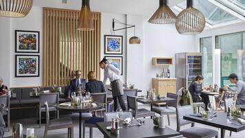 A modern dining area with round tables, pendant lighting, and artwork on the walls.