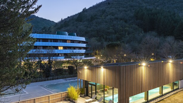 Um edifício moderno com piscina, espreguiçadeiras e vista para a floresta ao redor.