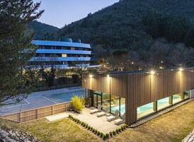 Un edificio moderno con piscina, sillas de descanso y vistas al bosque circundante.