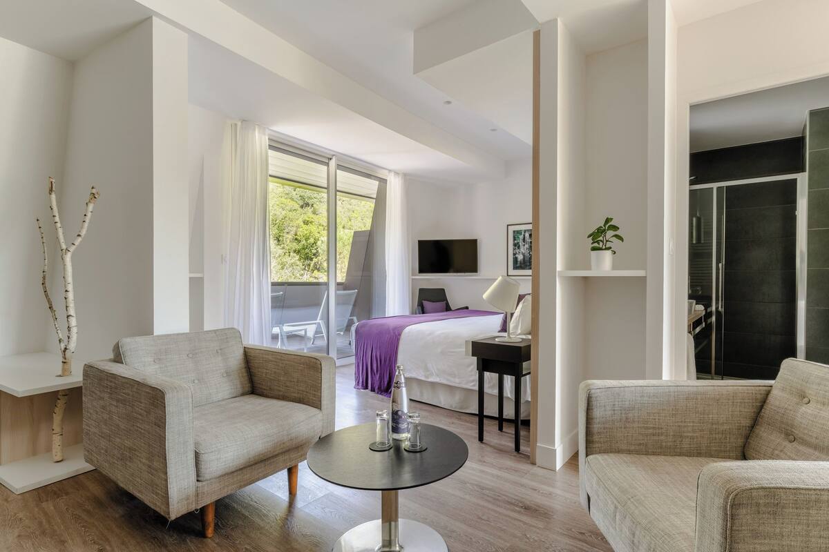A modern hotel room with a large bed, a sitting area with two sofas, a small table, and a TV.