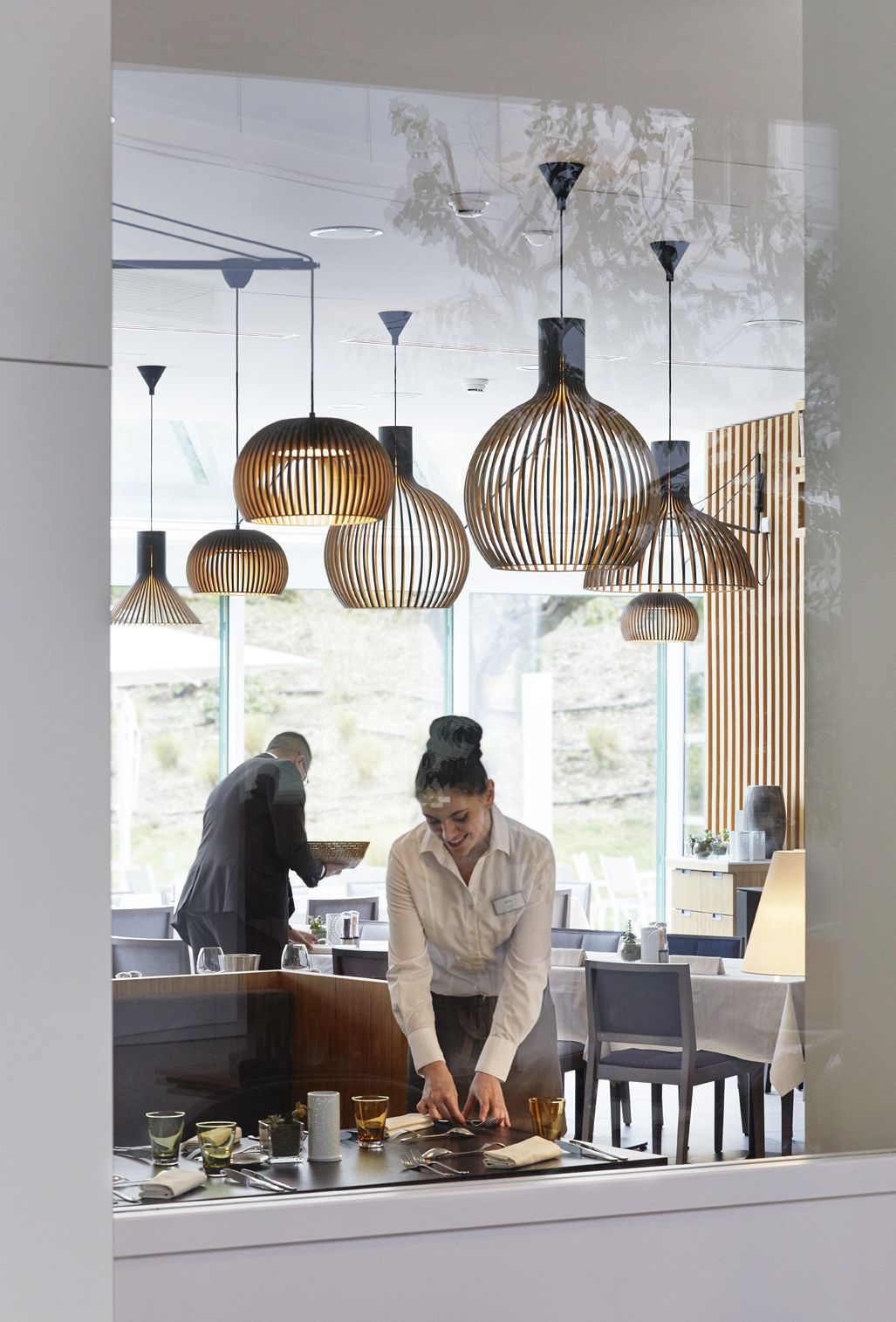 Een restaurantinterieur met moderne hanglampen, een eethoek en uitzicht op het omliggende landschap.