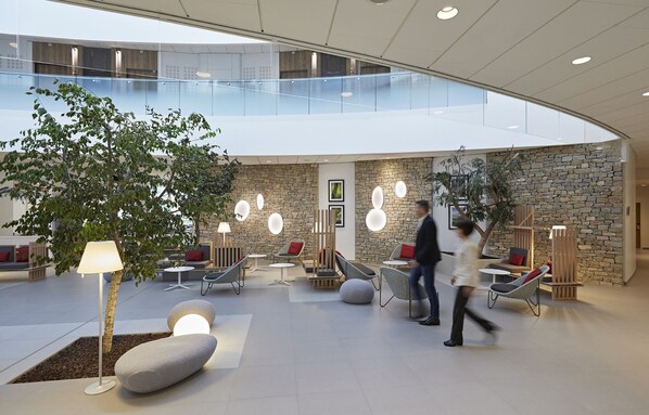 Un moderno vestíbulo interior con techo de cristal, paredes de piedra y zonas de estar contemporáneas.
