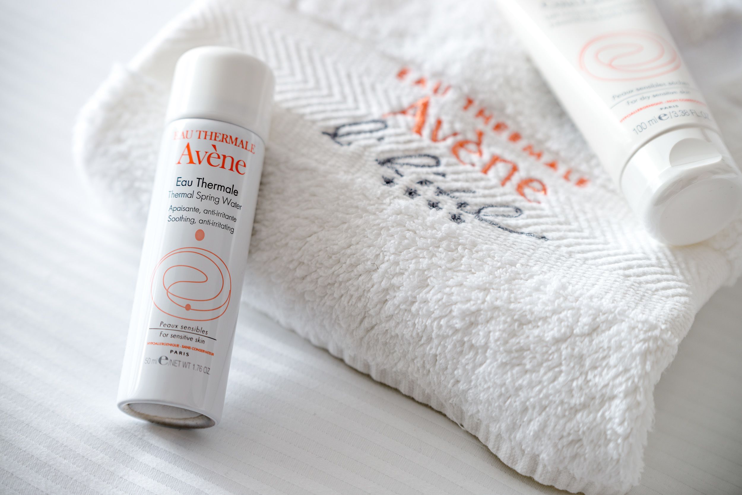 Une bouteille d’eau thermale Avène et une serviette blanche ornée du logo Avène.