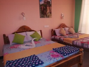 A room with two beds, each with a wooden headboard, a floral bedspread, and multiple pillows. There is a wall-mounted light fixture above each bed. - Sigiri La Veranda Lodge (Sigiriya)