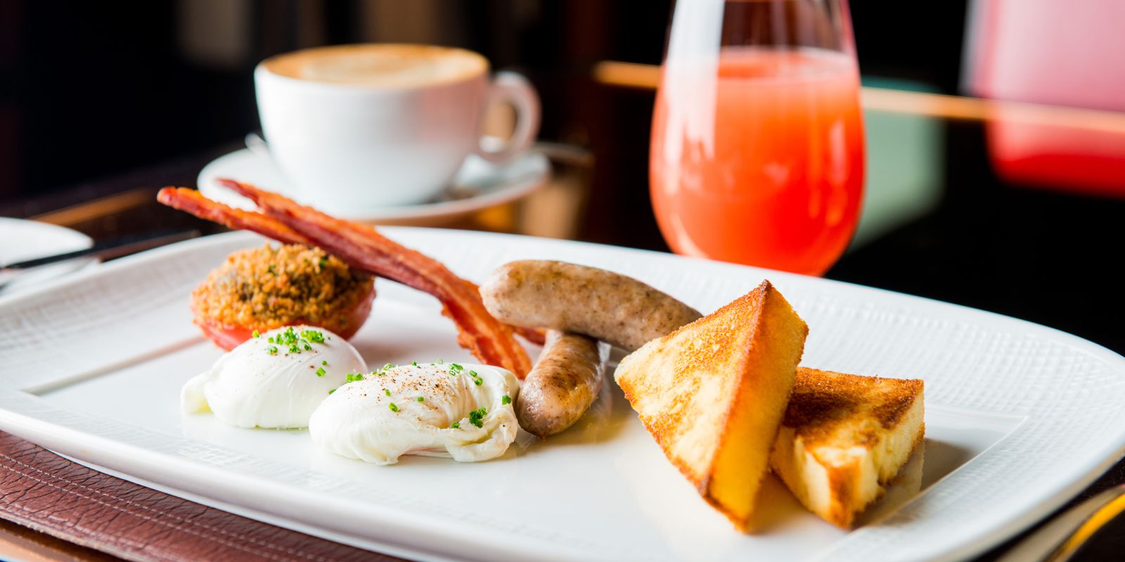 Un plato de desayuno con huevos, tocino, salchicha, tostadas y un muffin.