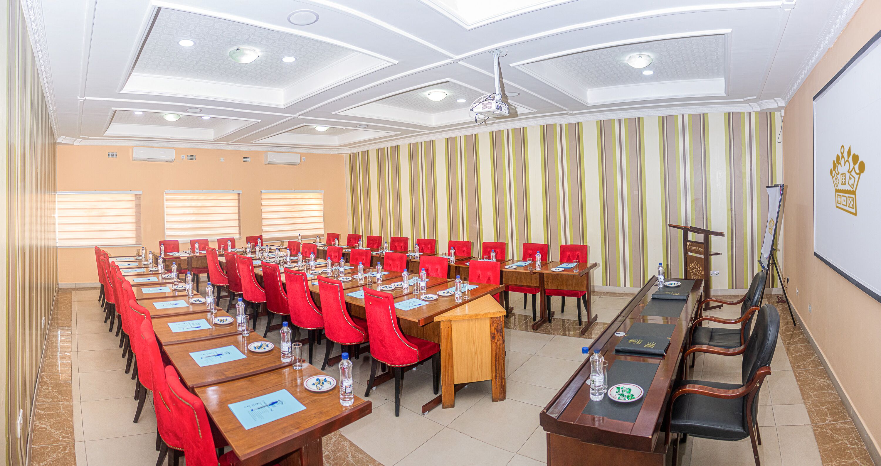 A conference room with multiple tables, red chairs, and a projector screen.