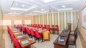 A conference room with multiple tables, red chairs, and a projector screen.