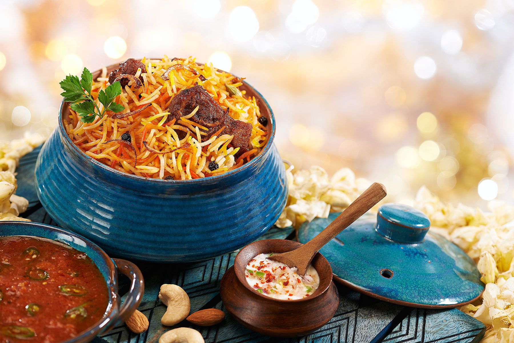 A bowl of biryani with meat and vegetables, a small bowl of sauce, and a wooden spoon.