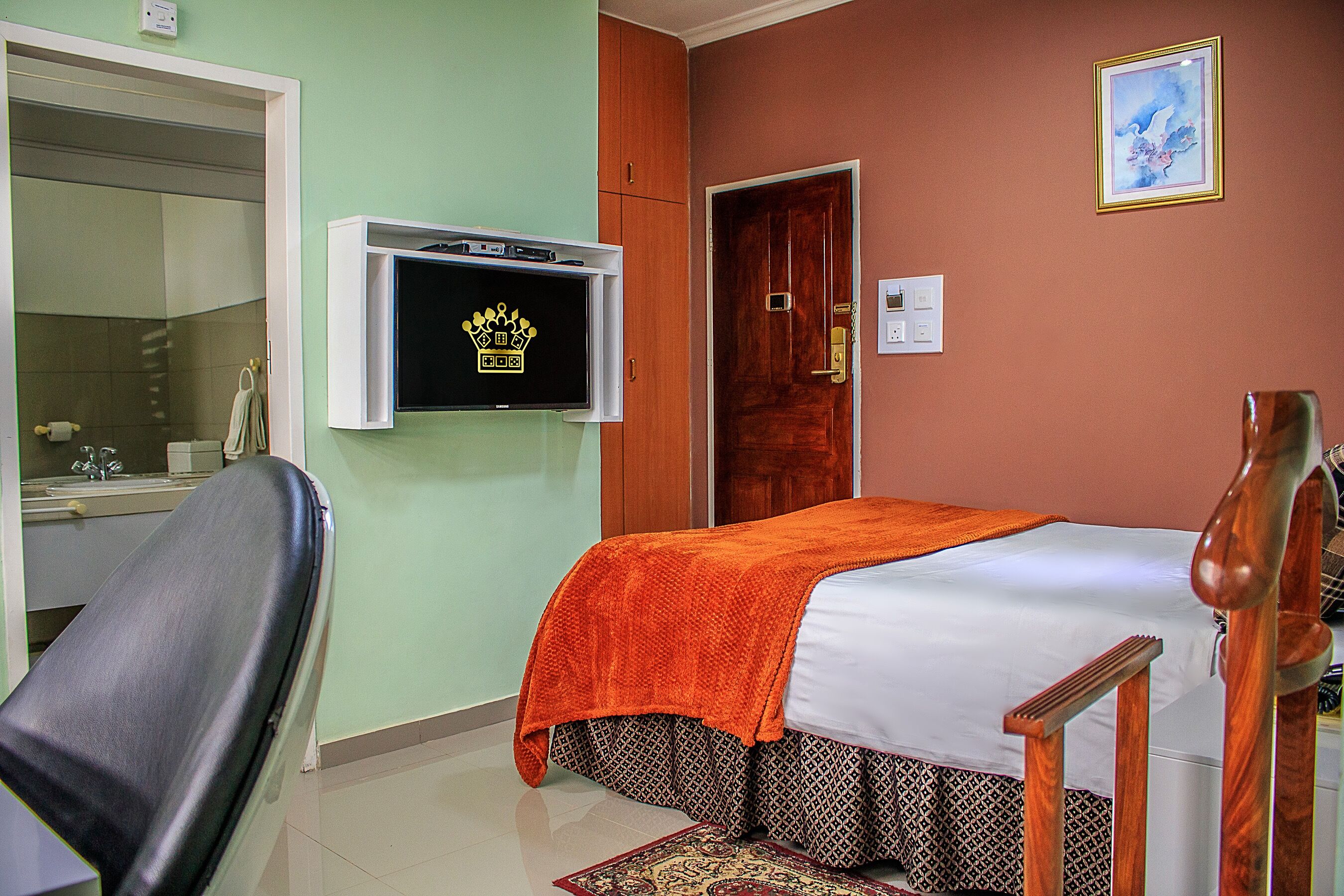A hotel room with a bed, a television mounted on the wall, a wooden chair, and a door.