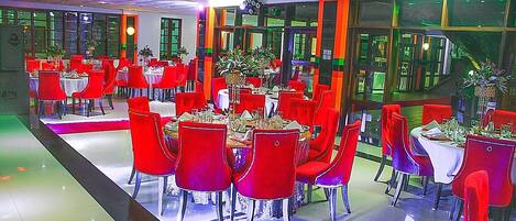 A dining area with multiple tables and chairs, arranged in a spacious layout with large windows allowing natural light.