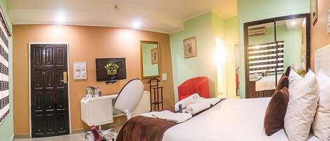 A hotel room with a bed, a desk, a chair, a TV, and a minibar.
