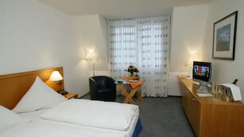 Ein Hotelzimmer mit Bett, Schreibtisch, Stuhl, Fernseher und einem gerahmten Bild an der Wand.