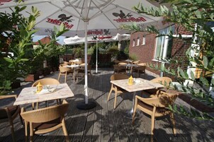 Un patio al aire libre con mesas, sillas, sombrillas y plantas en macetas.