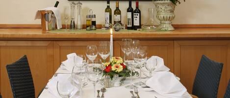 A dining table set for a meal with a white tablecloth, wine bottles, glasses, and a vase with flowers.