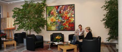 A lobby with black leather sofas, a large floral painting, and potted plants.