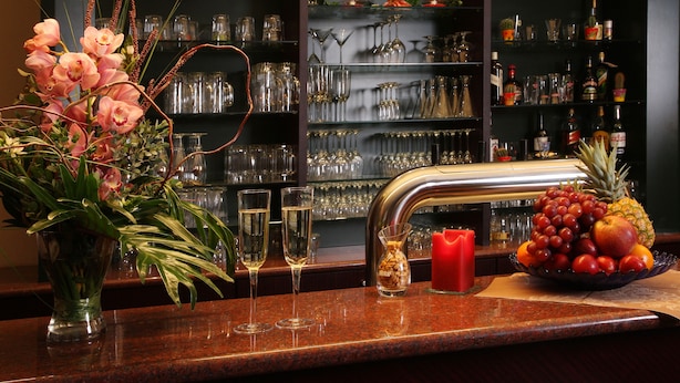 A bar area with a wine glass display, a fruit bowl, and a vase of flowers. - Stadthotel Oranienburg (Oranienburg)