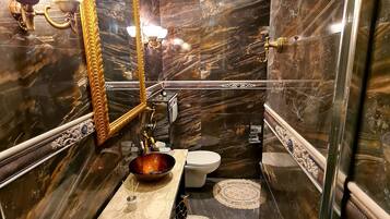 Ein luxuriöses Badezimmer mit dunklen Marmorwänden, einem großen Spiegel, einem Waschbecken und zwei runden Teppichen auf dem Boden.