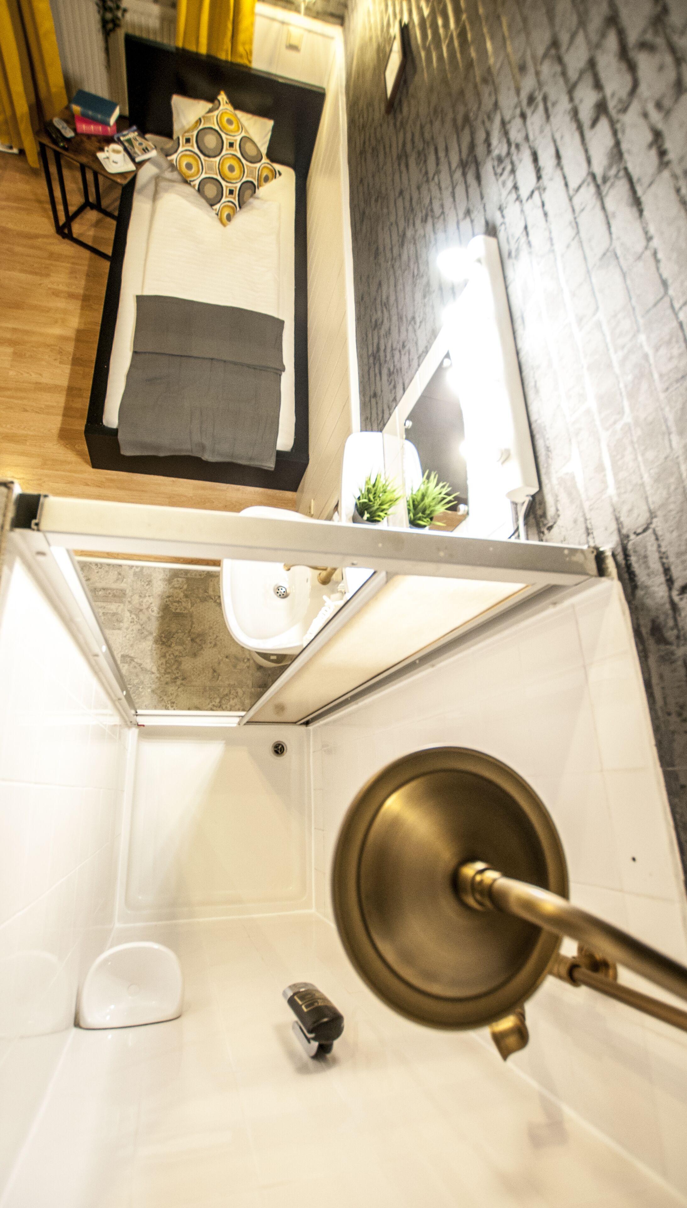 Baño con inodoro, lavabo y ducha. Hay una cama con almohadas y una mesita de noche con libros y un teléfono.