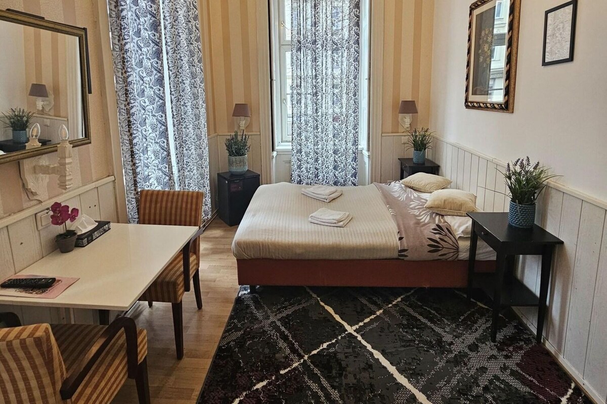 Un dormitorio con cama, escritorio, silla, espejo, candelabro y ventana con cortinas.