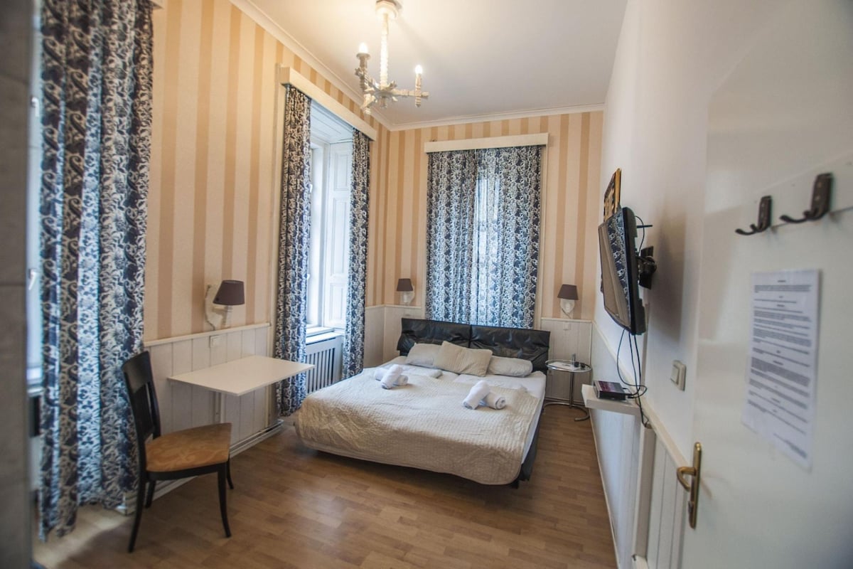 Una habitación de hotel con cama, escritorio, silla, televisor y cortinas.