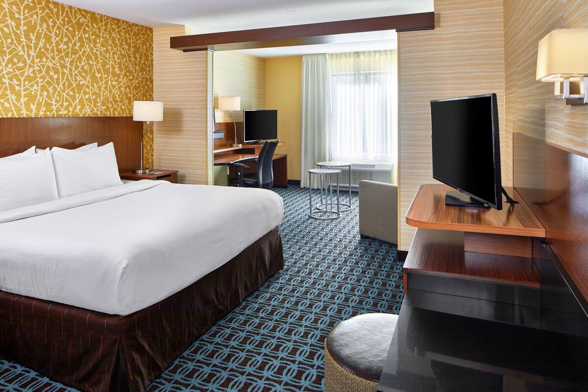 A hotel room with a large bed, a desk with a chair, a television, and a small table.