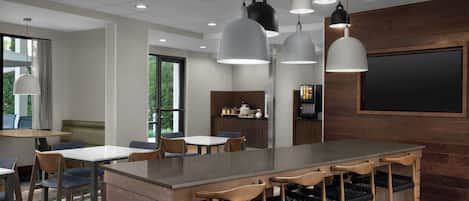 A modern bar area with a central island, bar stools, pendant lighting, and a large flat-screen TV mounted on the wall.