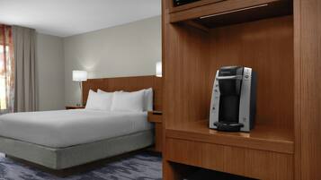 A hotel room with a bed, a nightstand, a lamp, and a Keurig coffee maker on a wooden shelf.