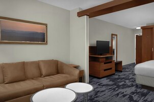 Una habitación de hotel con sofá, una mesita redonda, televisor, espejo y armario.