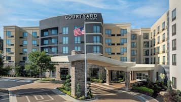 Un hotel Courtyard by Marriott con un diseño moderno, que presenta una destacada bandera estadounidense, una entrada cubierta y un camino de entrada ajardinado.