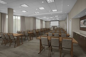 A conference room with multiple tables and chairs, a projector screen, and a large window with curtains. - Fairfield Inn & Suites Atlanta Lithia Springs (Lithia Springs)