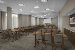 Un salón de conferencias con varias mesas y sillas, una pantalla de proyector y un ventanal con cortinas.
