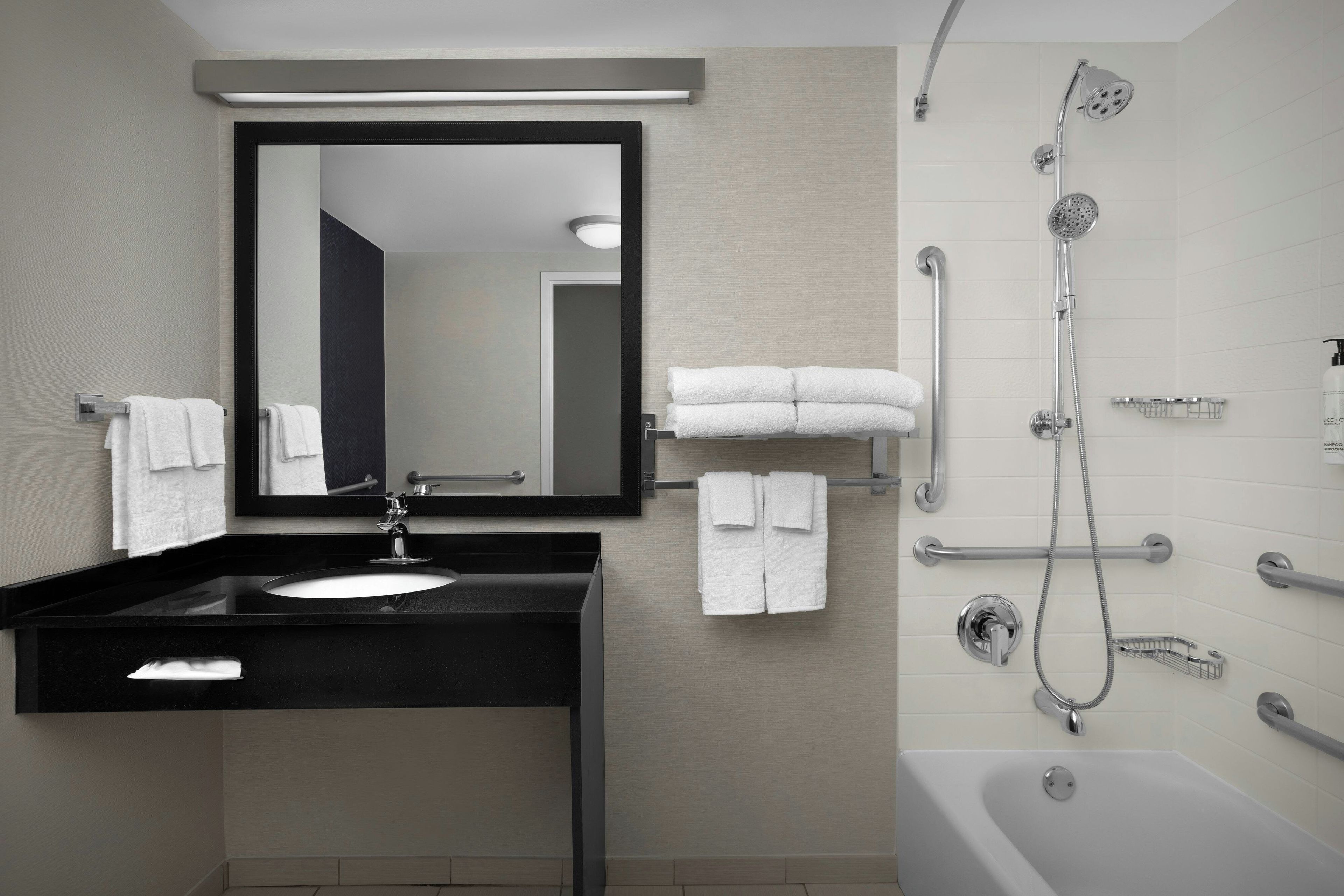 Un baño moderno con tocador negro, un espejo grande, una bañera y una ducha con varios controles.