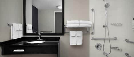 Un baño moderno con tocador negro, un espejo grande, una bañera y una ducha con varios controles.