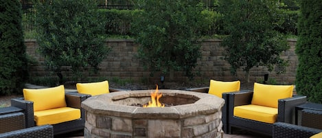 A stone fire pit surrounded by wicker furniture with yellow cushions.