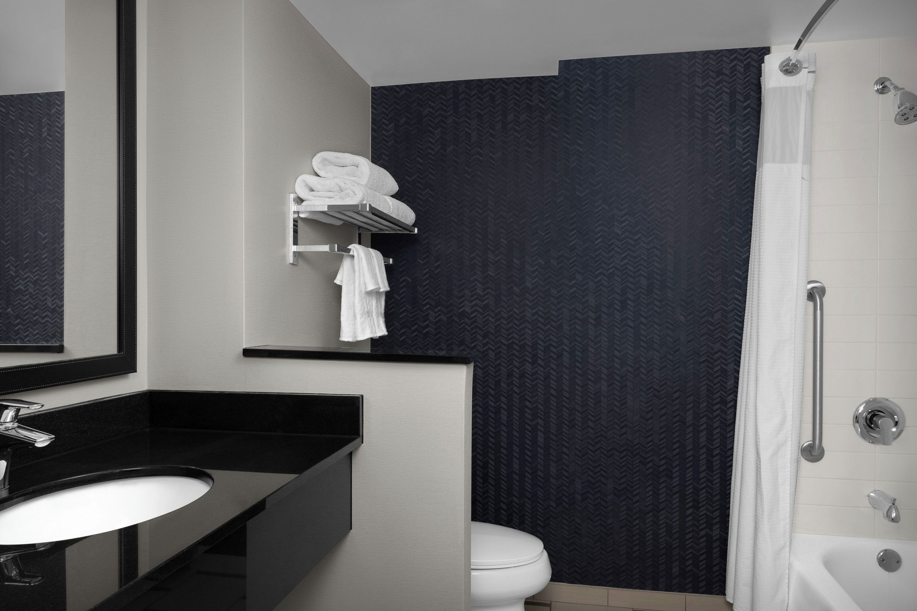 A bathroom with a black countertop sink, a mirror, a towel rack with towels, a white toilet, and a shower area.