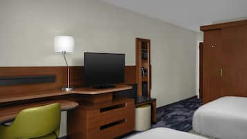 Une chambre d’hôtel avec un bureau en bois, une télévision, un fauteuil vert, une armoire et un lit.