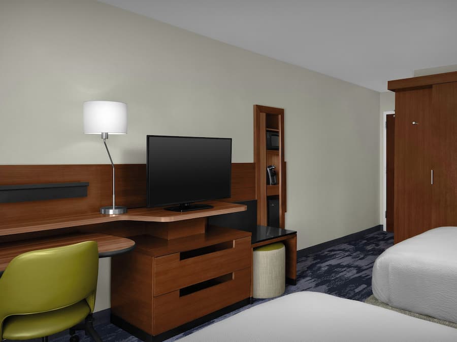 Une chambre d’hôtel avec un bureau en bois, une télévision, un fauteuil vert, une armoire et un lit.