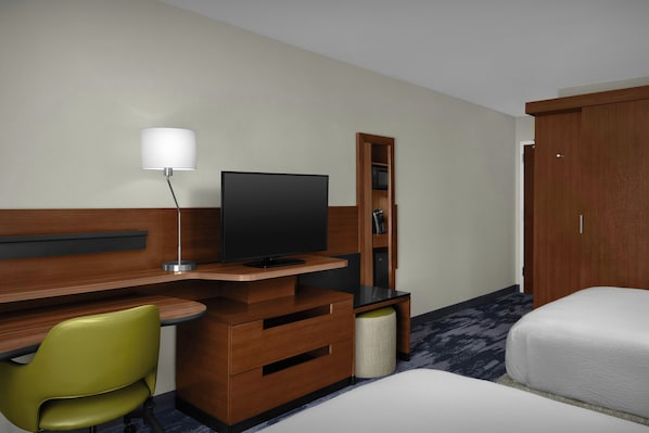 Une chambre d’hôtel avec un bureau en bois, une télévision, un fauteuil vert, une armoire et un lit.