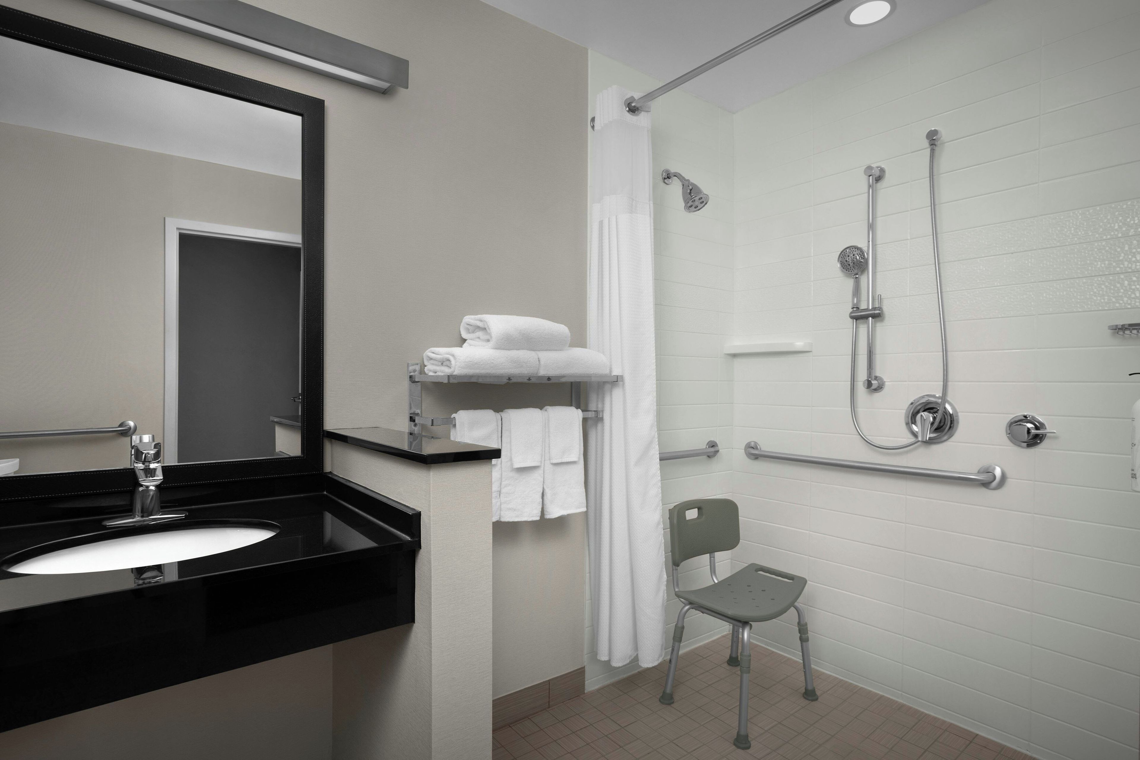 A modern bathroom with a black sink, a mirror, a shower with a handheld showerhead, and a grab bar.