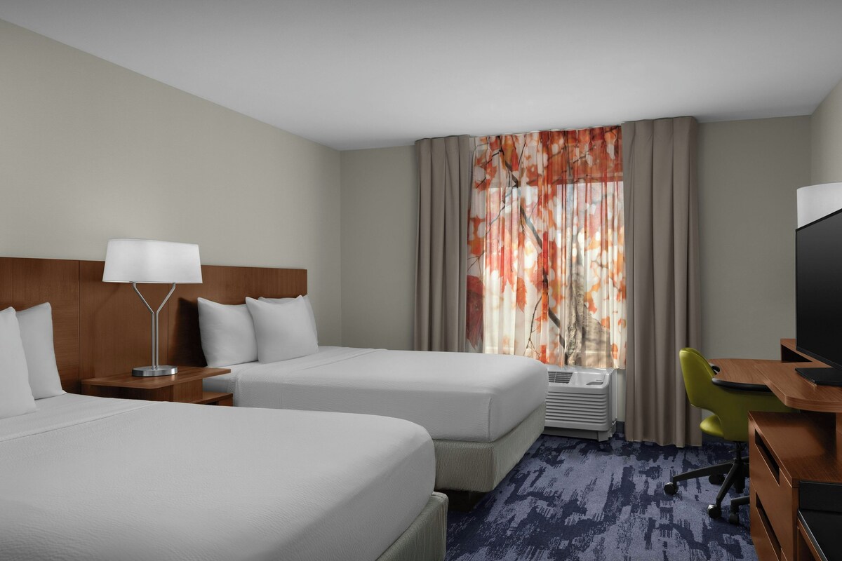 A hotel room with two beds, a desk, a chair, a television, and a window with curtains.