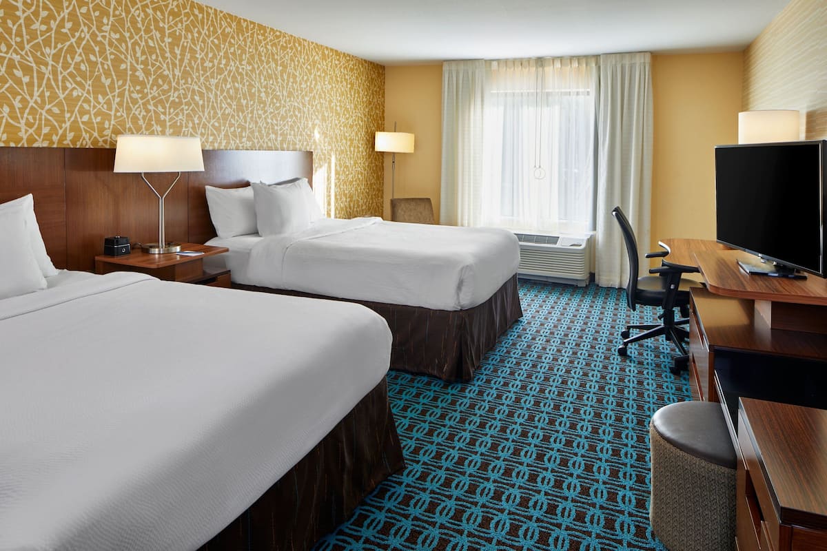 A hotel room with two beds, a desk, a TV, and a chair.