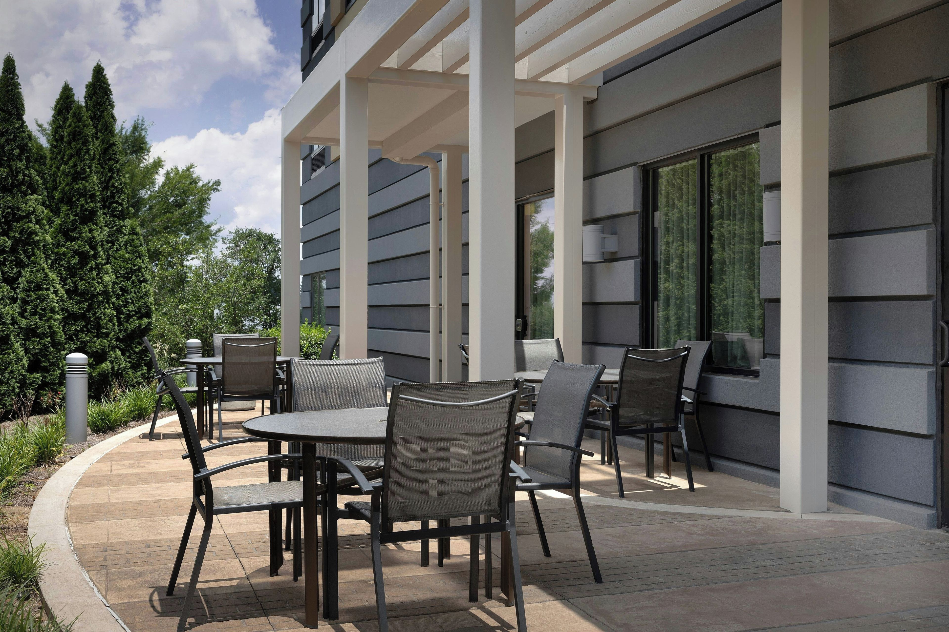 An outdoor patio with a table and chairs, surrounded by a building with large windows and a covered area.