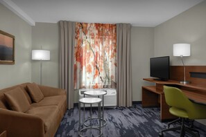 Ein Hotelzimmer mit einer Couch, einem Schreibtisch mit Computer, einem Fernseher und einem Sessel.