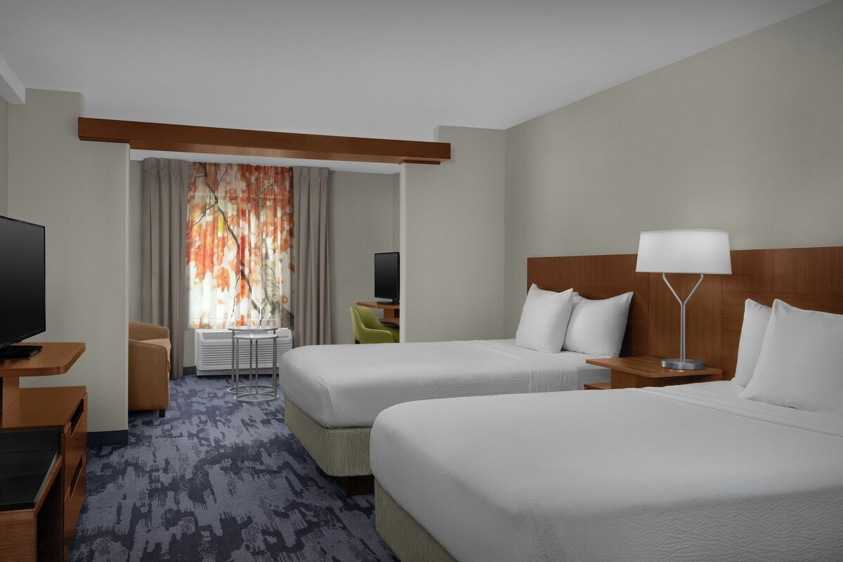 A hotel room with two beds, a desk, a television, and a lamp.