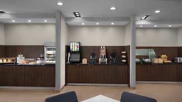 A modern cafe with a wooden counter, a coffee machine, a juice dispenser, and a variety of food items.