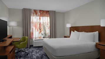 Quarto de hotel com cama, escrivaninha, cadeira, televisão e janela com cortinas.