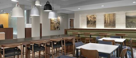 A modern restaurant interior with a long counter, multiple seating options, and pendant lighting.